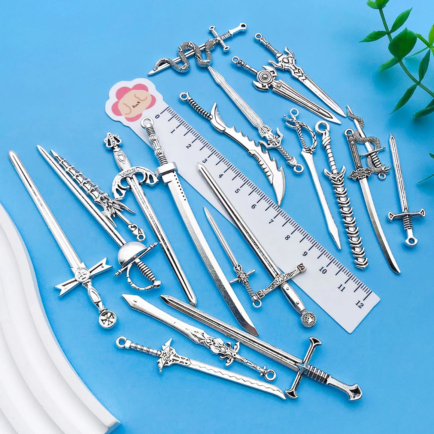 Collection of silver sword-shaped jewelry on a blue background with a ruler for scale.