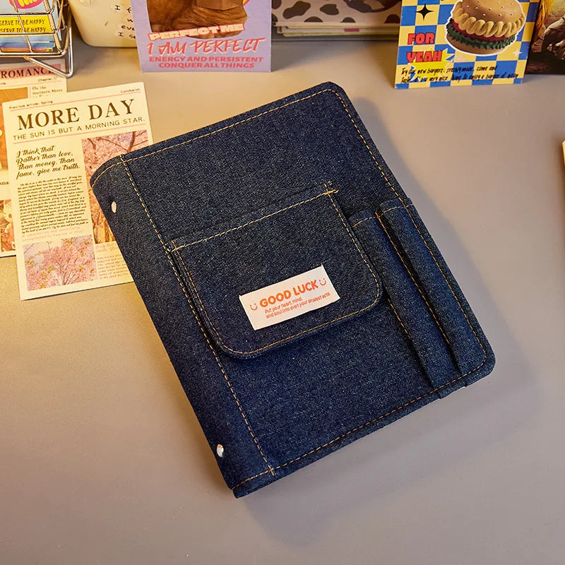 Blue denim notebook with a 'Good Luck' label on a light gray surface