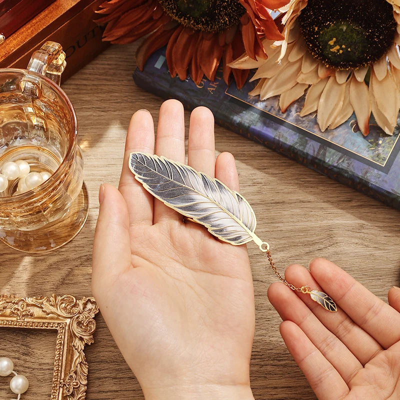 Feather-shaped jewelry on a hand with sunflowers and a glass in the background