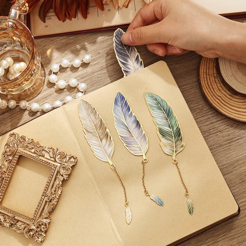 Decorative feather bookmarks on a notebook with a glass of water and pearls in the background.