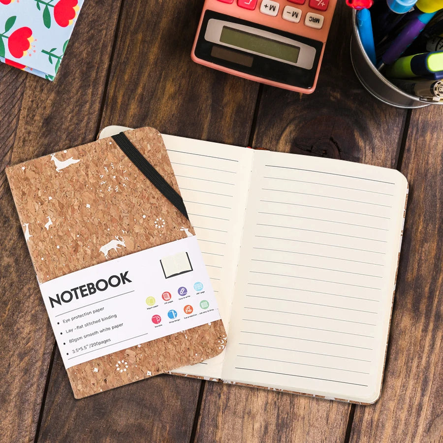 Open notebook with cork cover on a wooden surface with stationery items.