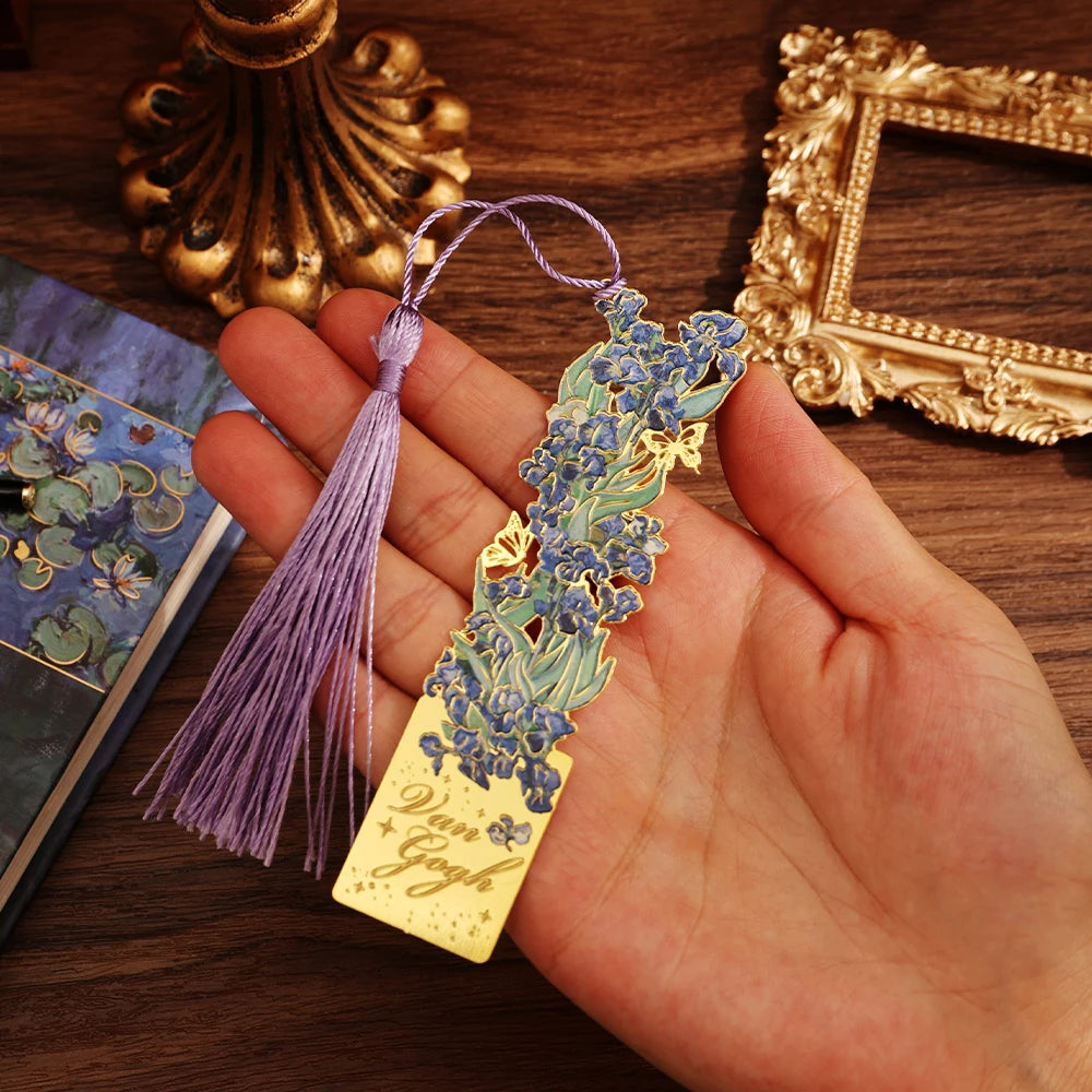 Decorative bookmark with floral design and tassel held by a hand on a wooden surface.