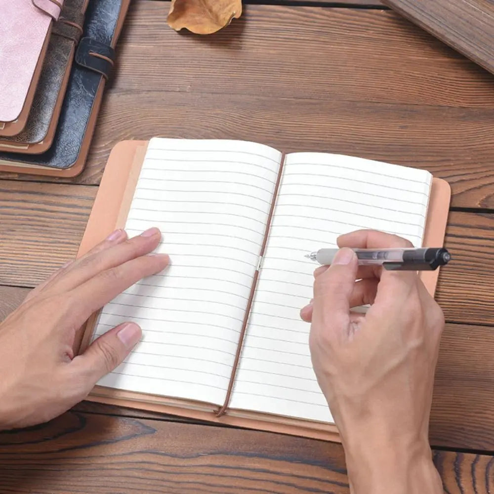 Person holding a pen over an open notebook on a wooden surface