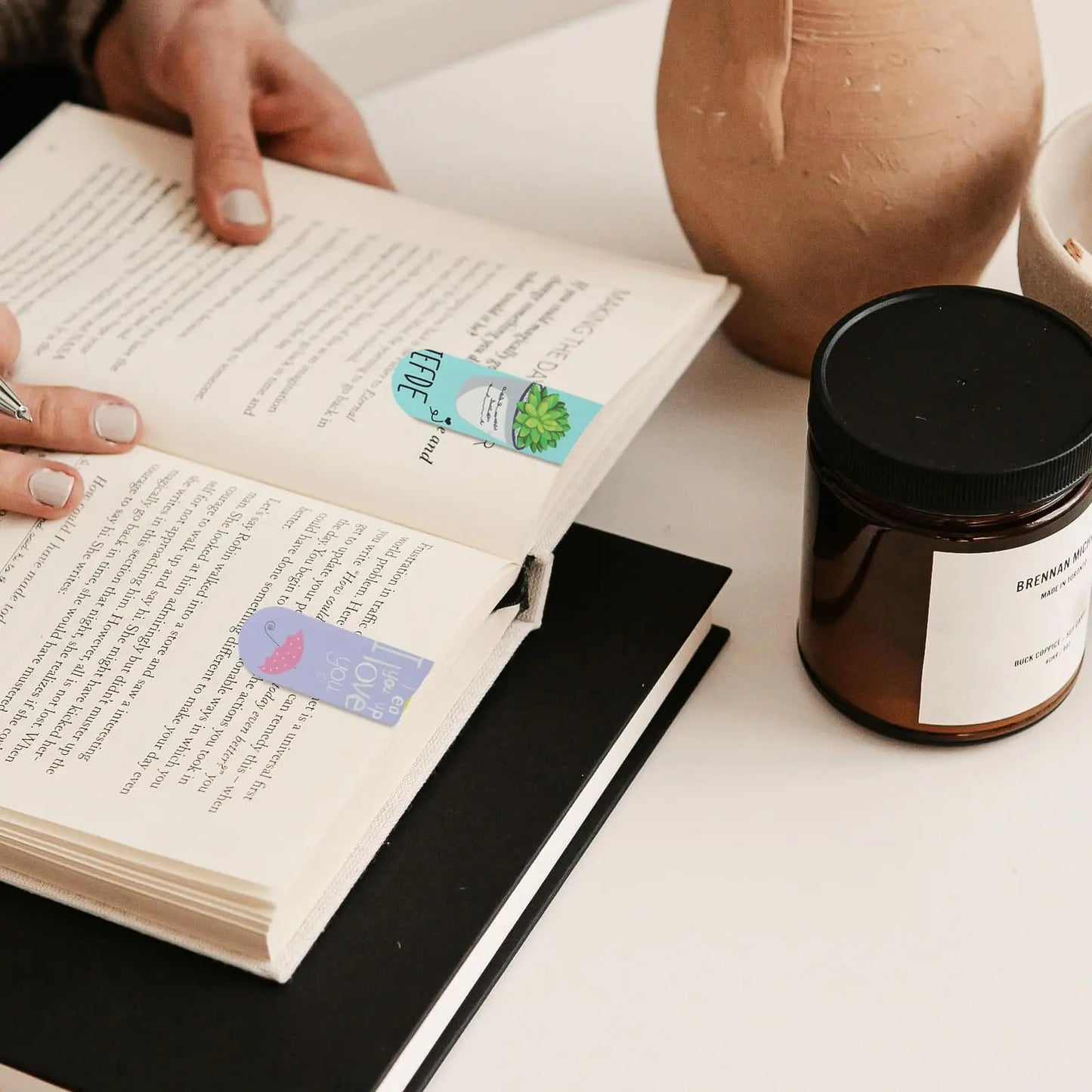 Open book with bookmarks and a jar on a table
