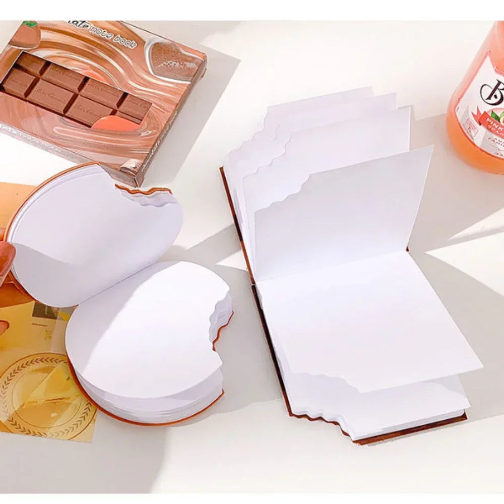 White paper stacks on a white surface with a box of chocolate and a bottle of orange juice in the background.