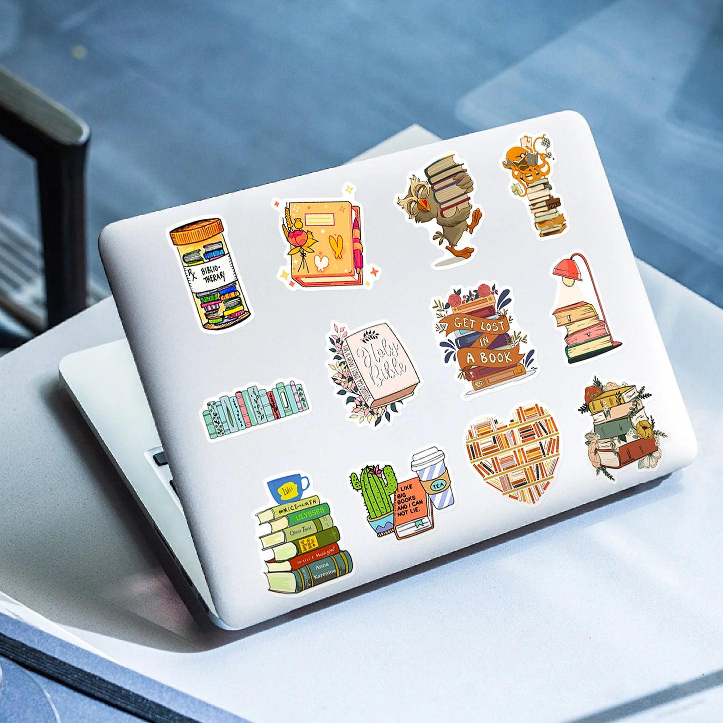 Laptop with book-themed stickers on a glass table