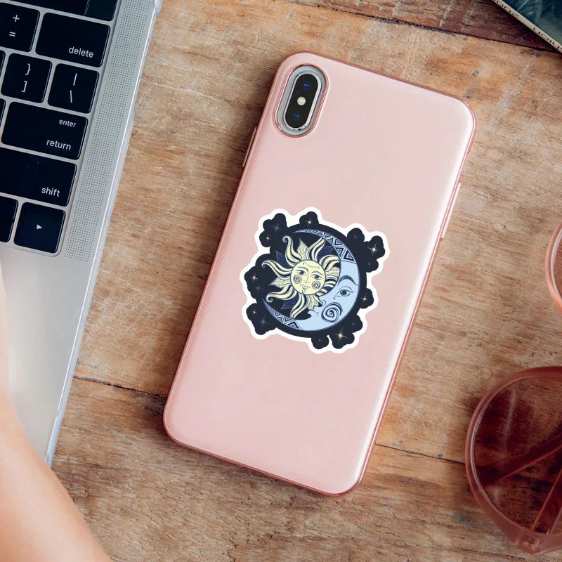 Pink phone with a decorative sticker on a wooden surface next to a laptop.