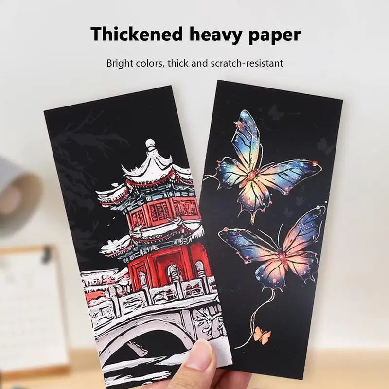 Two pieces of thick paper with designs of a pagoda and butterflies, held by a hand.