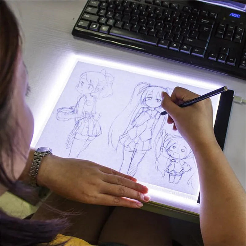 Person drawing anime characters on a light pad with a keyboard in the background