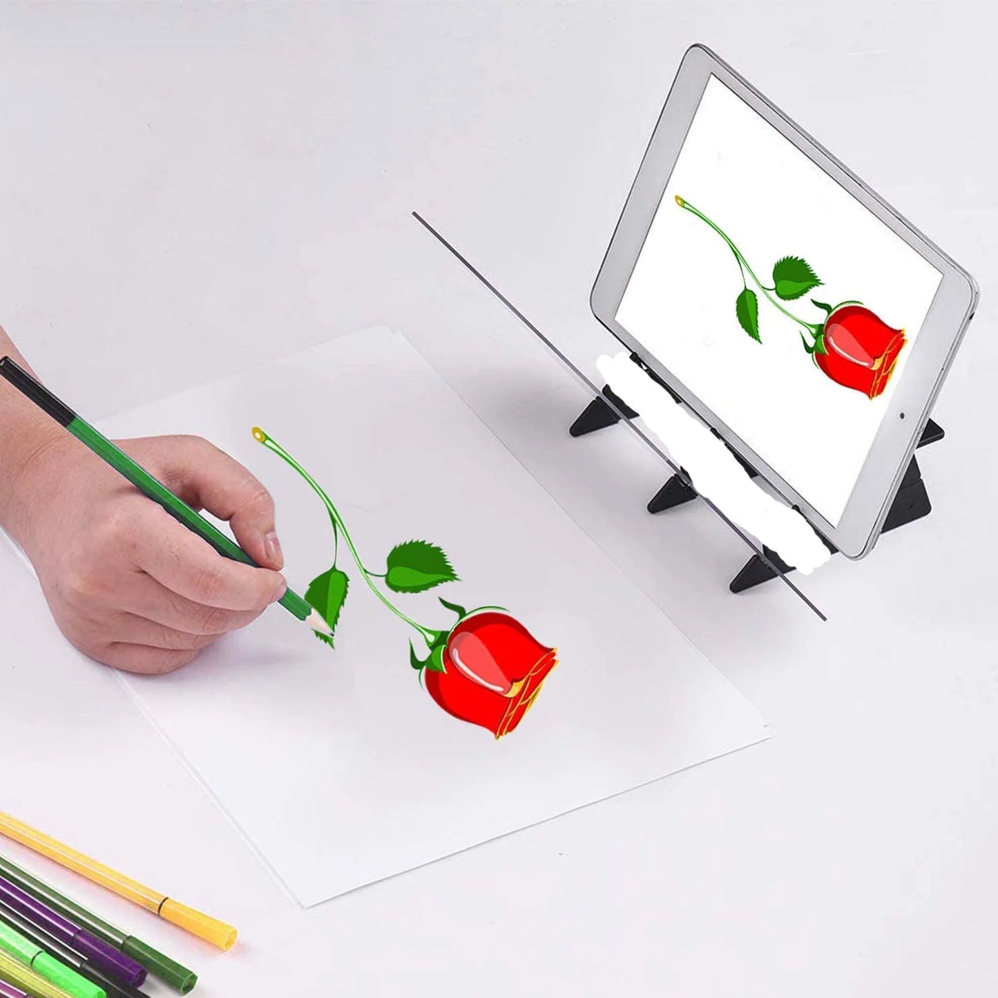 Hand drawing a red rose on paper with a tablet displaying a similar image.