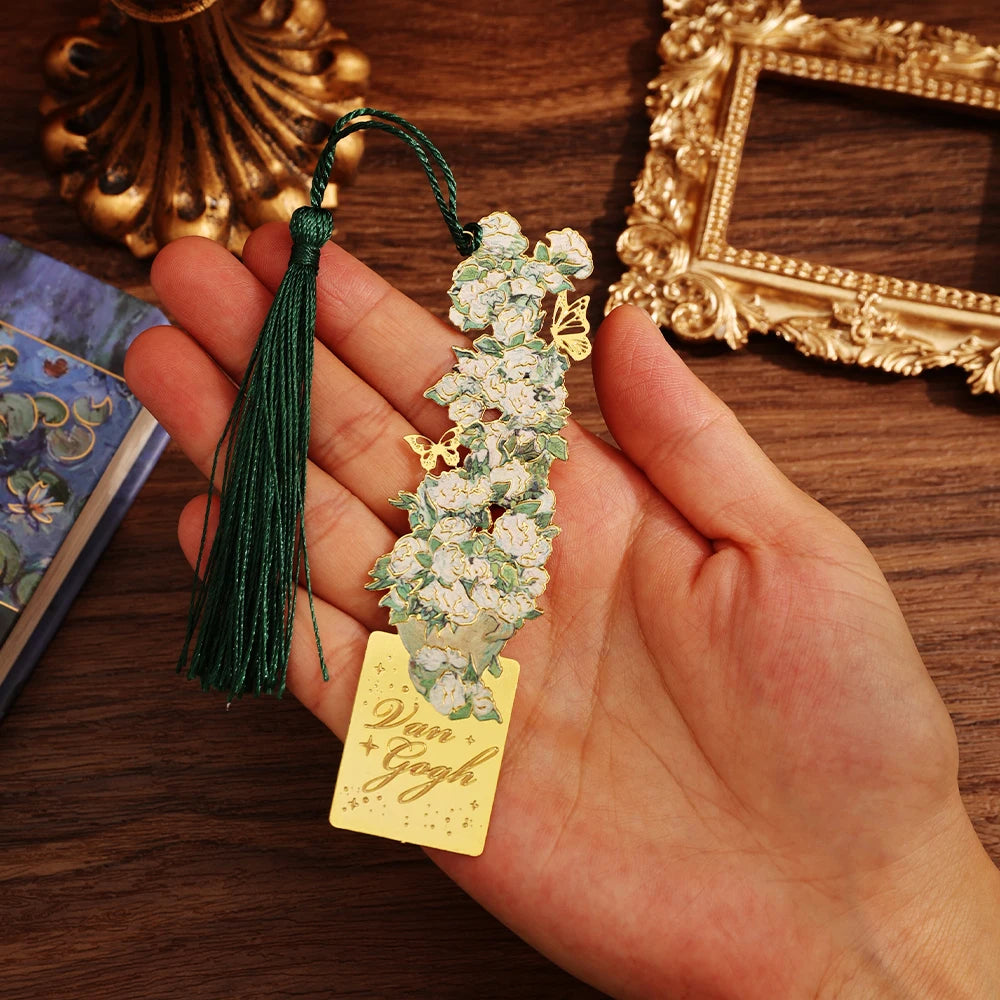 Hand holding a decorative bookmark with floral design and 'Van Gogh' tag on a wooden surface.