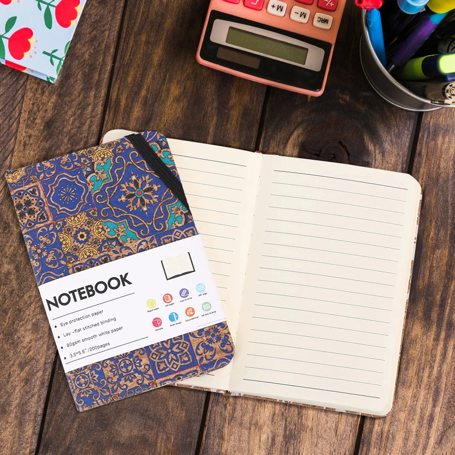 Open notebook with decorative cover on a wooden surface with stationery items.