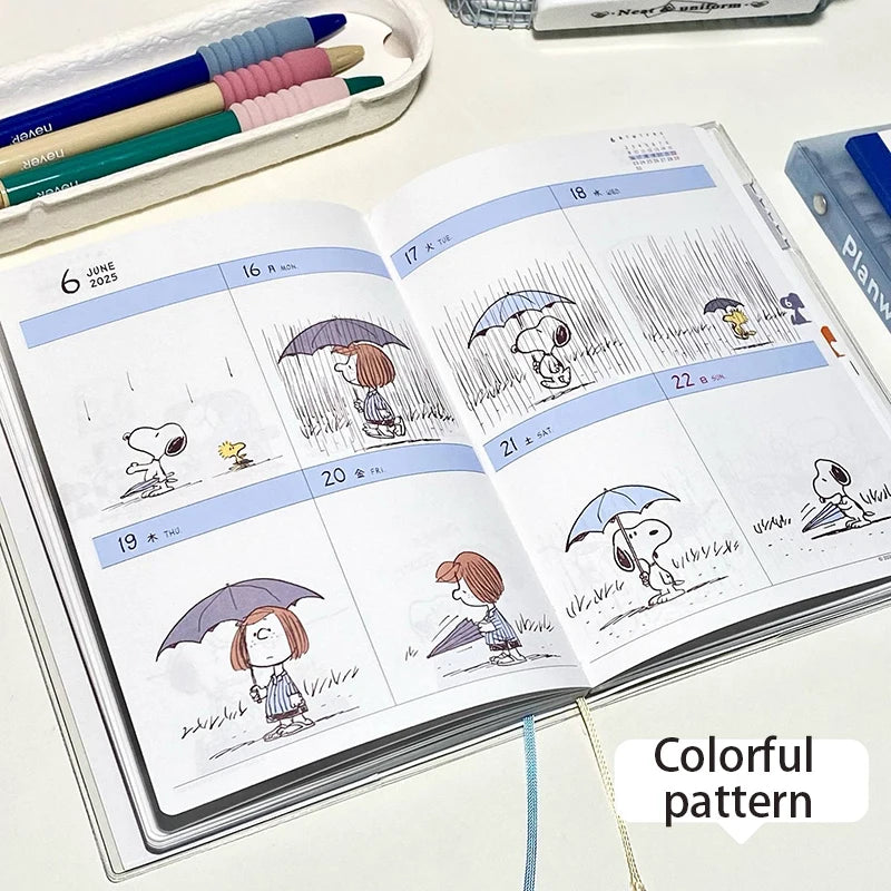 Open planner with cartoon illustrations of Snoopy and Woodstock holding umbrellas, with a colorful pattern on a white surface.