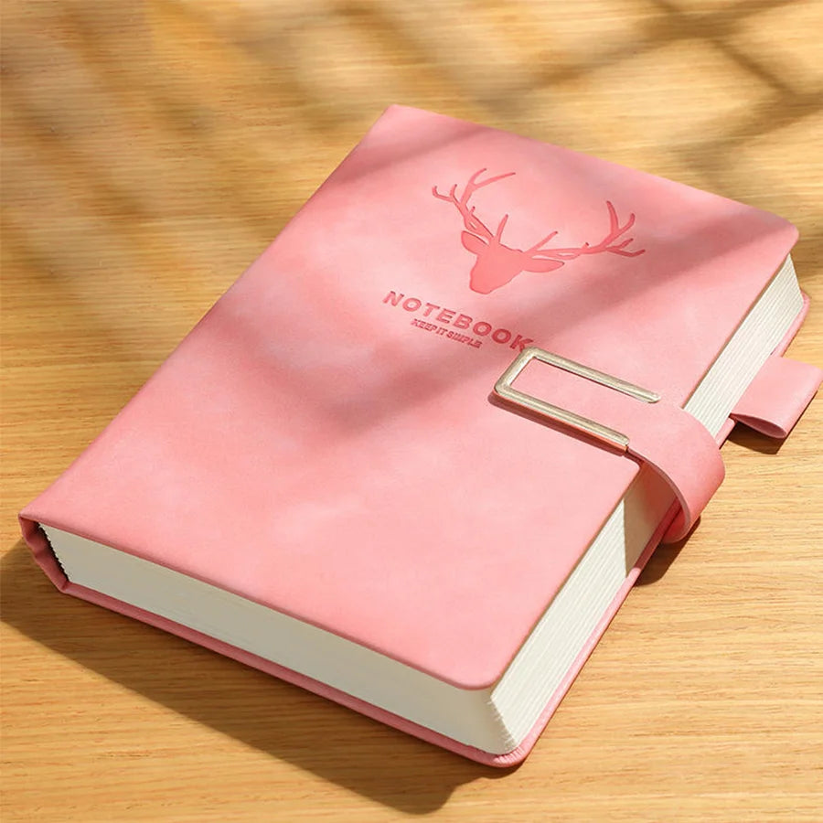 Pink notebook with deer design on the cover, placed on a wooden surface.