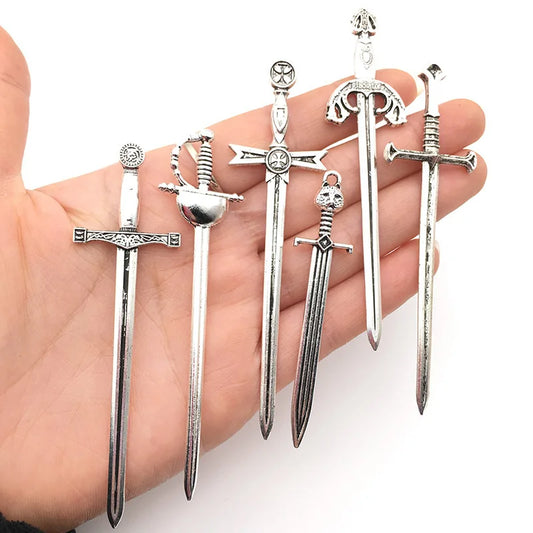 A set of six metal Antiqued  bookmarks shaped like antique swords, held in a person's hand. Each bookmark has a different design, featuring details such as crosses and pointed tips.