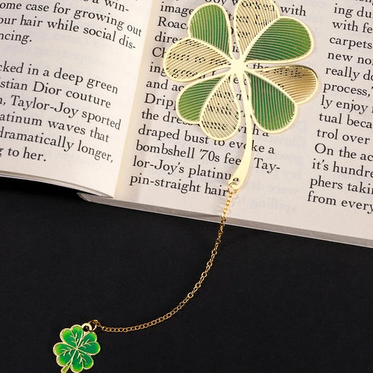 A metal bookmark designed like a four leaf clover with green and gold colors, laying on an open book.