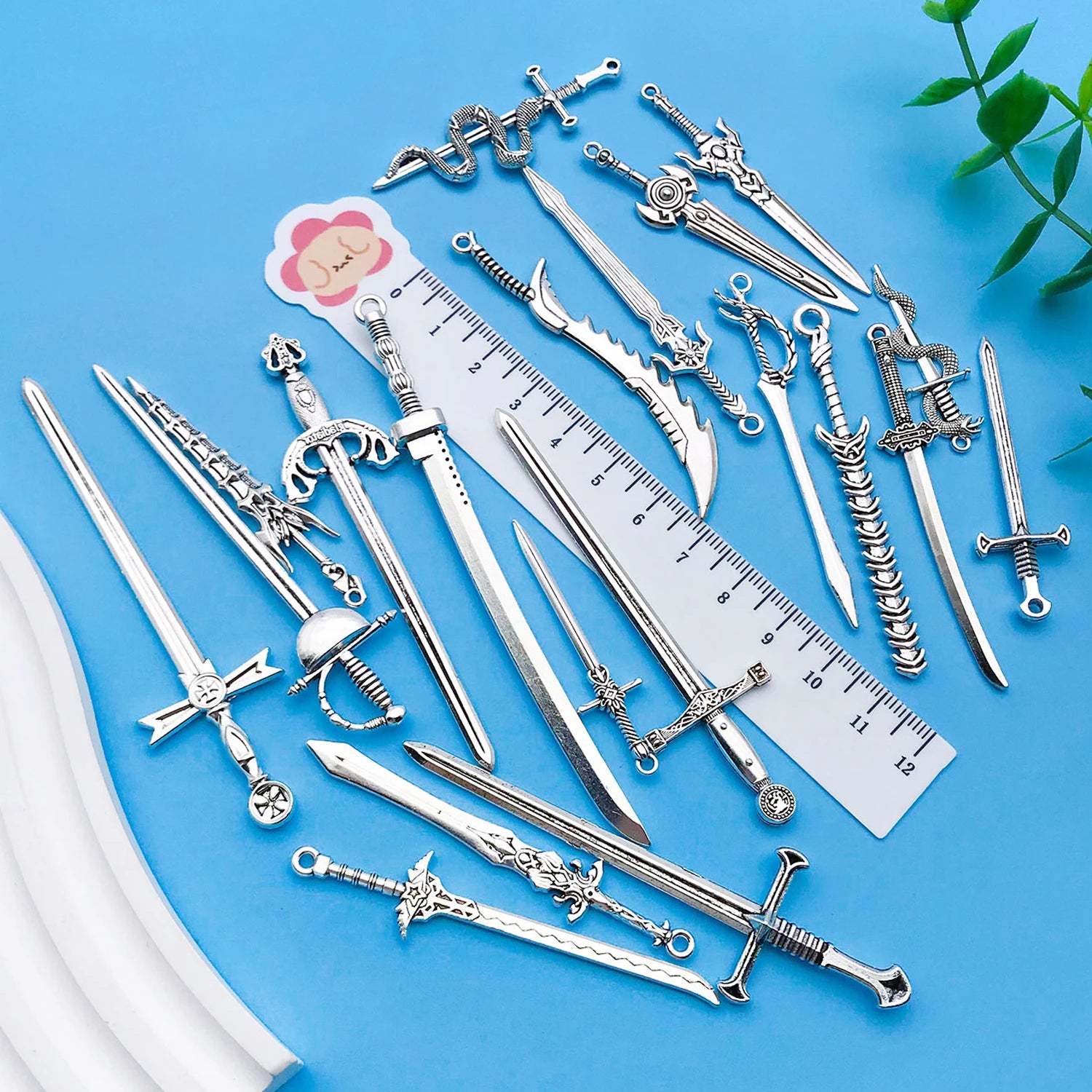 Collection of silver sword-shaped jewelry on a blue background with a ruler for scale.