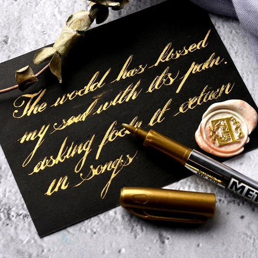 Black card with gold calligraphy, MEK pen, and wax seal on a gray surface.