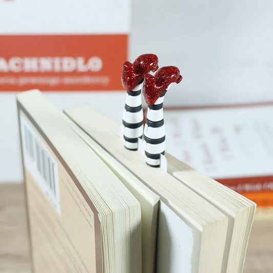 A pair of plastic bookmarks designed to look like high heels, placed on an open book.
