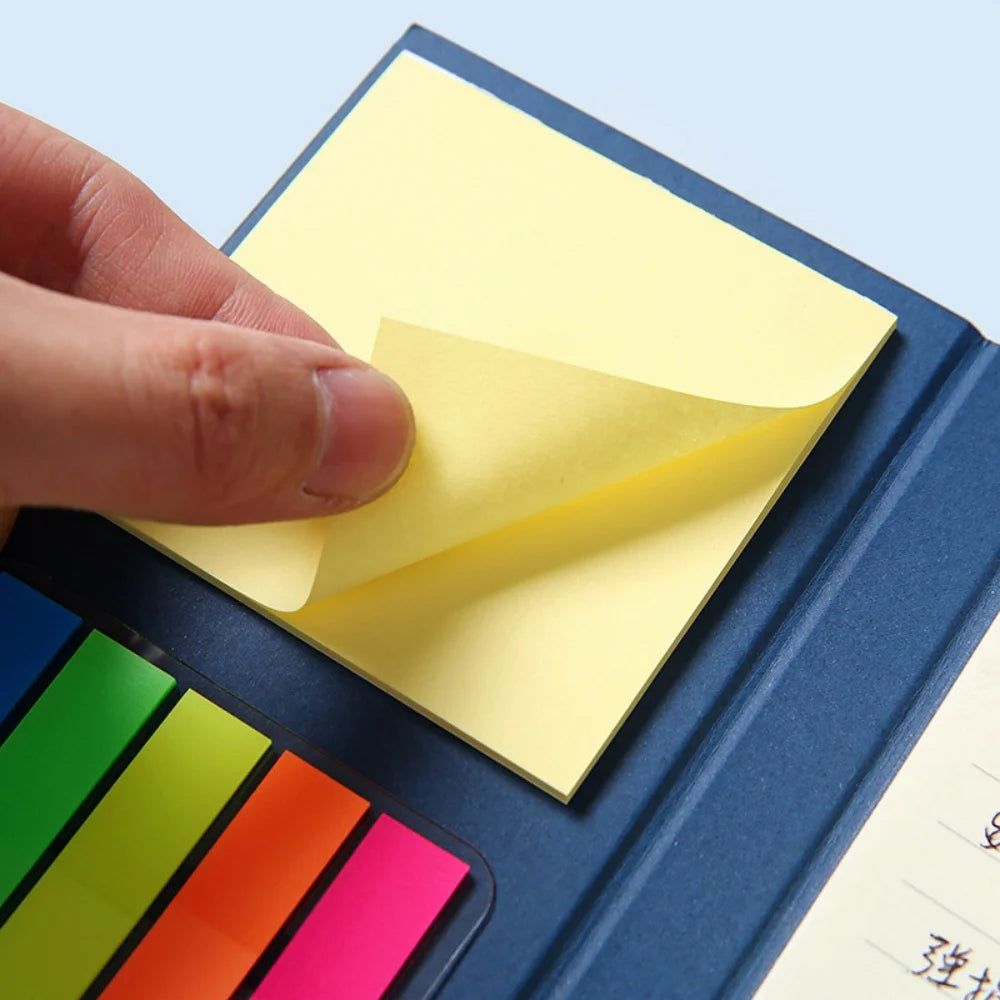 Hand placing a yellow sticky note on a blue notebook with colorful tabs.