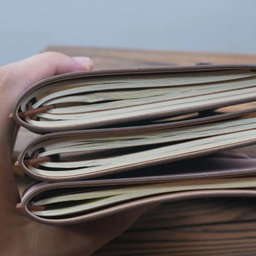 Hand holding a leather-bound notebook with open pages.