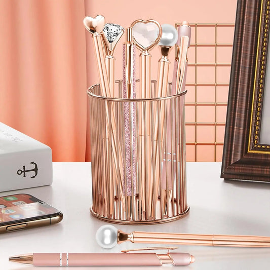 Rose gold decorative pens  in a cylindrical holder on a desk with a phone and decorative items.