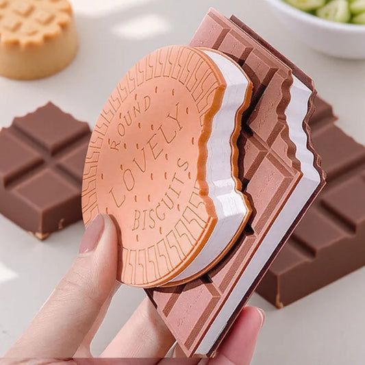 Chocolate bar with a biscuit design held by a hand, surrounded by cookies and chocolate pieces.