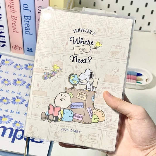 Hand holding a 2023 diary with Snoopy design and text 'Traveler's Where to Next?' on a white background.