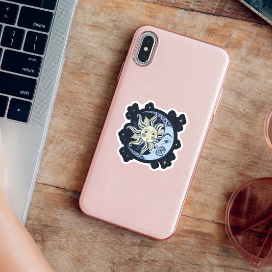 Pink phone with a decorative sticker on a wooden surface next to a laptop.