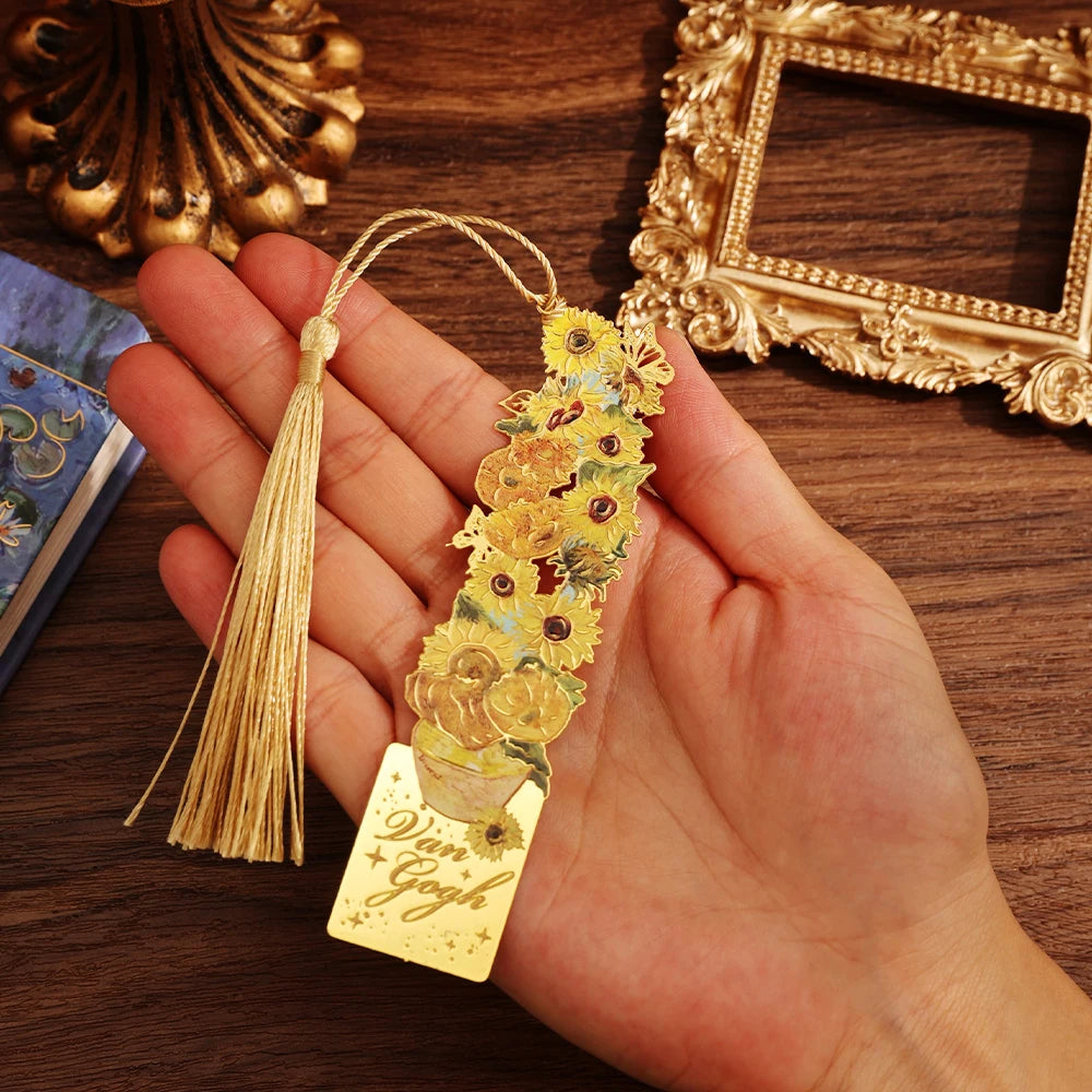Gold bookmark with floral design held by a hand on a wooden surface