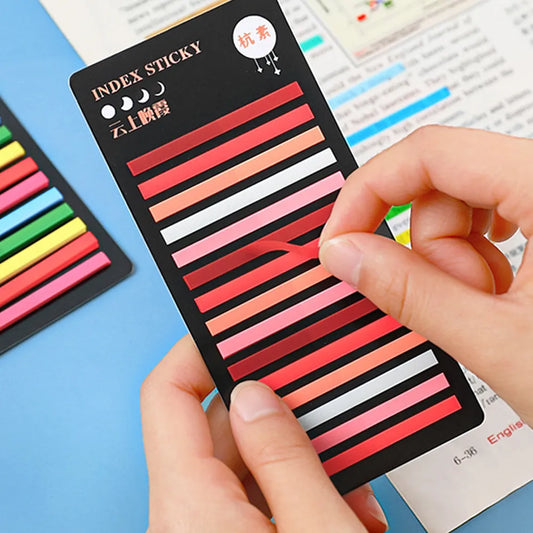 A hand holding a transparent rainbow index pad with adhesive notes, from which a selection of colorful sticky notes are visible.