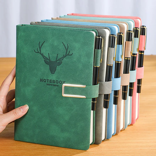Green notebook with deer emblem held by a hand, surrounded by other notebooks in various colors on a wooden surface.
