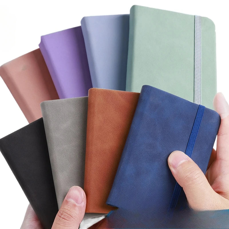 Hand holding a blue notebook with other notebooks in various colors on a white background